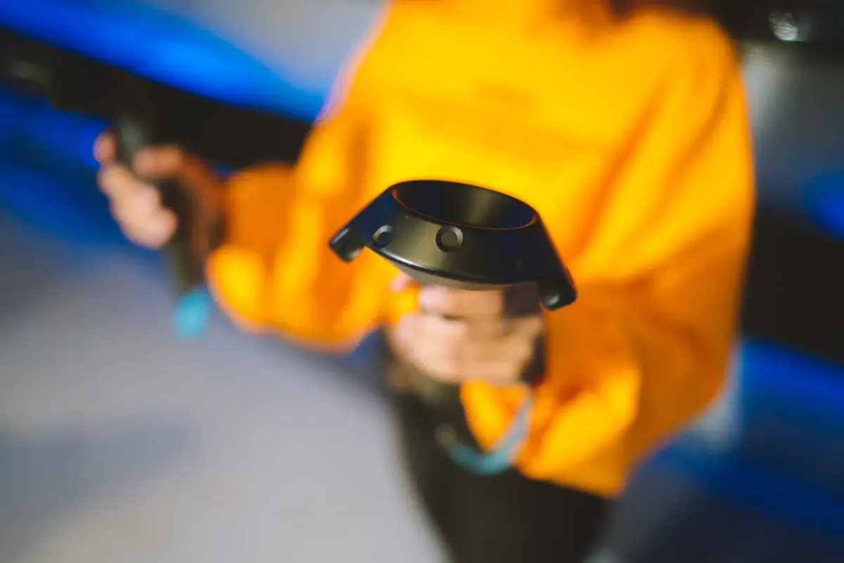 A person in a yellow sweater holds two virtual reality controllers in a blue-lit room