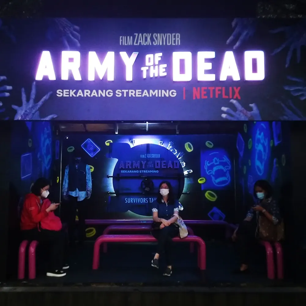 Halte bus bertema film Army of the Dead dari Netflix dengan papan nama menyala dan dekorasi neon pada malam hari
