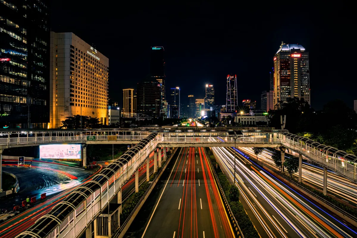Jalan protokol Jakarta pada malam hari dengan jejak lampu kendaraan dan gedung tinggi