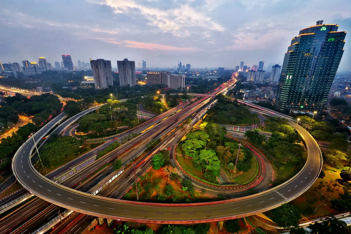 Elevated highway interchange in Jakarta at dusk with vehicle light trails and high-rise buildings behind