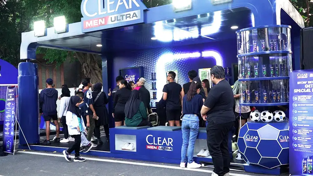 A blue football-themed brand activation booth by the roadside, with visitors gathered in front of the product display under floodlights