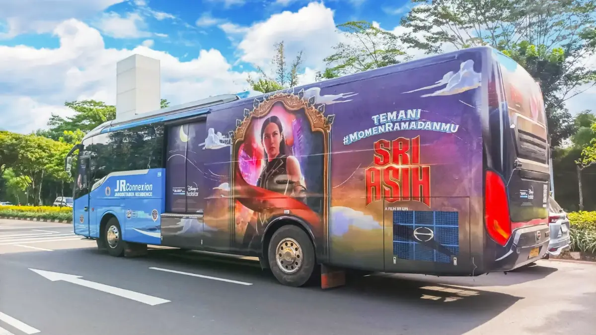 Bus Transjabodetabek berstiker penuh kampanye film Sri Asih dari Disney melintas di jalan pada siang hari